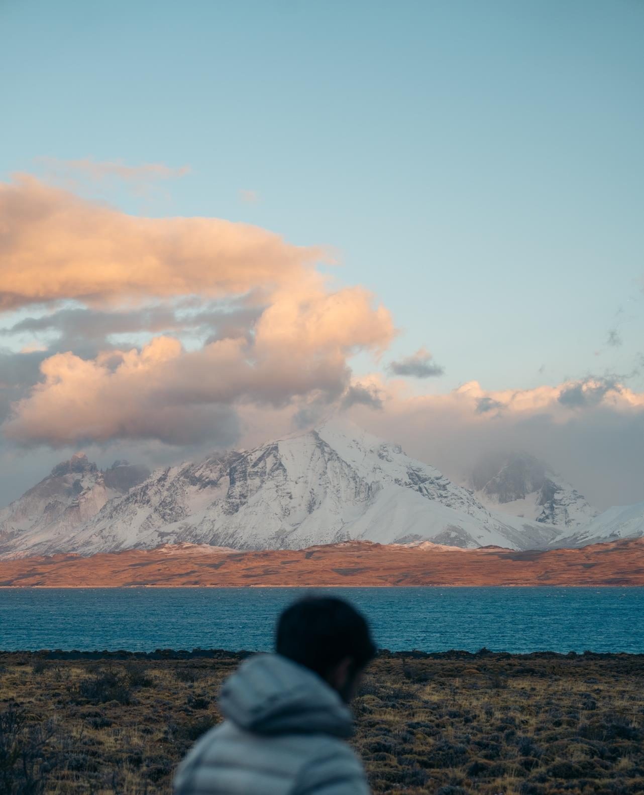 A traveller facing a Patagonian lake with snow-capped mountains and golden clouds